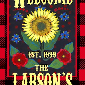 May include: Welcome sign with a black background and red and black checkered border. The sign features a yellow sunflower with green leaves, red flowers, and blue flowers. The text on the sign reads "Welcome, Est. 1999, The Larson's".