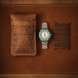 May include: A brown leather pouch with a textured crocodile pattern, a silver-tone wristwatch with a white dial and a green rotating bezel, and a rectangular brown leather card holder with a matching crocodile texture.