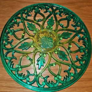 Puede incluir: Un tapiz decorativo de pared verde y dorado con un diseño circular que presenta intrincados patrones florales y un centro tipo mandala.