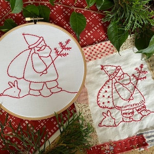 May include: Two embroidered images of Santa Claus with a bunny rabbit and a pine tree. The embroidery is done in red thread on white fabric. One image is in a wooden embroidery hoop.
