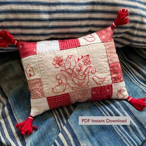 Può includere: Un cuscino patchwork rettangolare con quadrati di tessuto rossi e bianchi e motivi ricamati in rosso raffiguranti fiori, uccelli e conigli. Il cuscino presenta nappe di filo rosso su ogni angolo e include il testo PDF Instant Download.