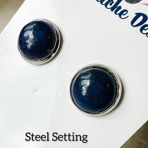 Peut inclure: Une paire de boucles d'oreilles en pierres précieuses bleu foncé avec des montures argentées. Les boucles d'oreilles sont présentées sur une carte blanche avec le texte "La Touche Des" et "Steel Setting".