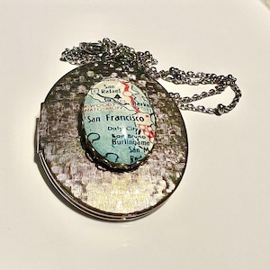 May include: A gold locket necklace with a round, glass charm featuring a vintage map of San Francisco. The map shows the city's neighborhoods and surrounding areas.