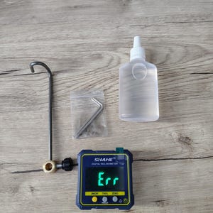 May include: A digital inclinometer with the text "Err" displayed on the screen, a clear plastic bottle, a metal tool, and a small bag with a metal tool. The inclinometer is blue and yellow.