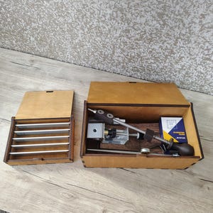 May include: Wooden knife sharpening system with a wooden box containing sharpening stones and a sharpening tool. The open box reveals the sharpening tool, a small box of sharpening oil, and other components.
