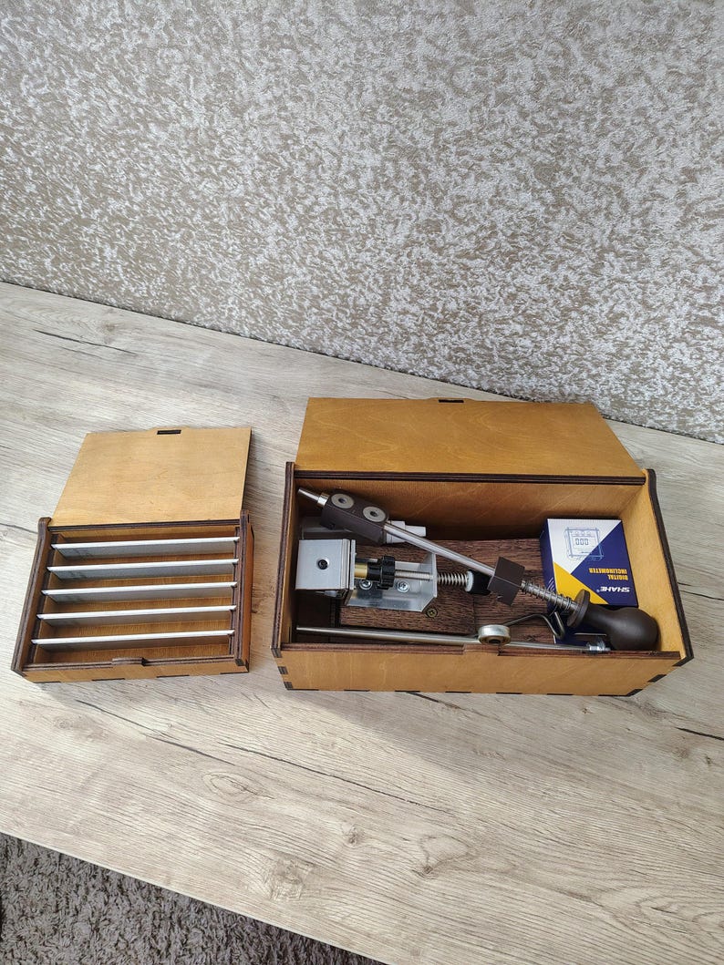 May include: Wooden knife sharpening system with a wooden box containing sharpening stones and a sharpening tool. The open box reveals the sharpening tool, a small box of sharpening oil, and other components.