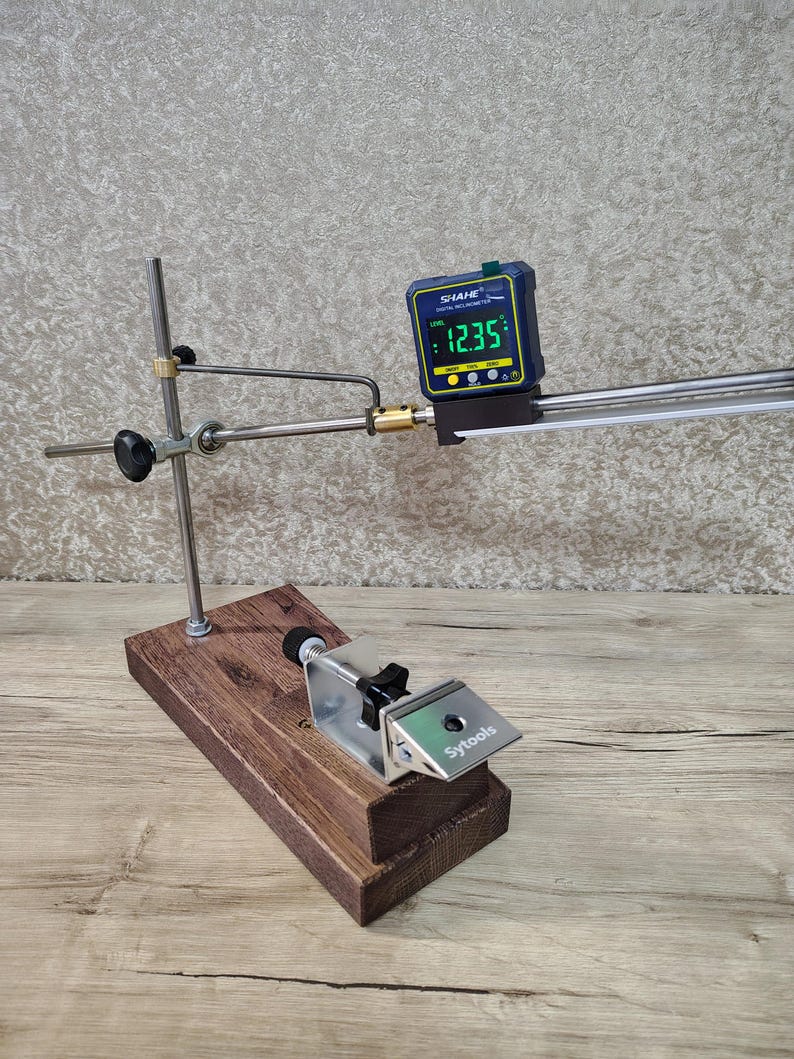 May include: A wooden and metal sharpening system with a digital inclinometer displaying 12.35 degrees. The system includes a base, a clamp, and adjustable arms. The brand name "Sytools" is visible on the clamp.