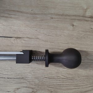 May include: A black, manual meat tenderizer tool with a silver metal rod, a black square block, a silver spring, and a black ball-shaped handle. The tool is designed to tenderize meat.