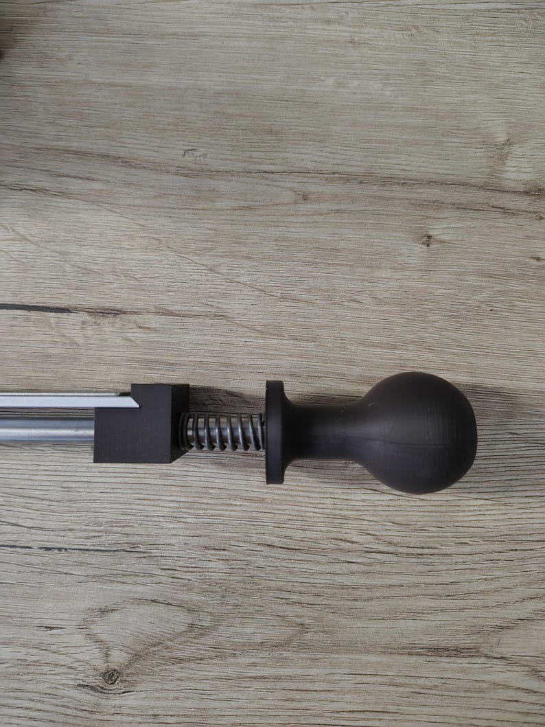 May include: A black, manual meat tenderizer tool with a silver metal rod, a black square block, a silver spring, and a black ball-shaped handle. The tool is designed to tenderize meat.