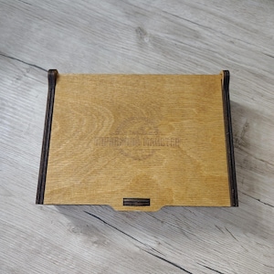 May include: A rectangular wooden box with a light brown top and dark brown edges. The box has a small rectangular indentation on the front. The text "ПРАВИЛА МАСТЕРА" is visible on the top.