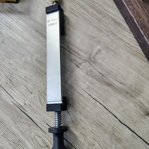 May include: A silver and black knife sharpener with the text "SY Tools 1500 #" printed on the blade. The sharpener has a black handle and a silver blade. The tool is designed for sharpening knives.