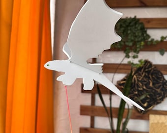 May include: White wooden dragon mobile hanging from the ceiling. The dragon is painted white and has a yellow and red string attached to it.