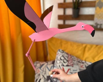 May include: A pink flamingo mobile with black and brown wings. The flamingo is suspended from the ceiling with a string and is in flight.