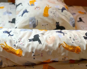 May include: A cream-colored bedding set with a playful cat design. The bedding features black, orange, and pink cats with various expressions and poses. The cats are surrounded by small details like milk cartons, paw prints, and hearts.