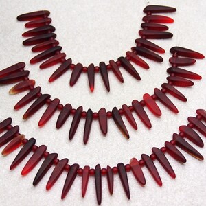 May include: Three strands of red glass beads, each strand is made up of teardrop-shaped beads with pointed tips.