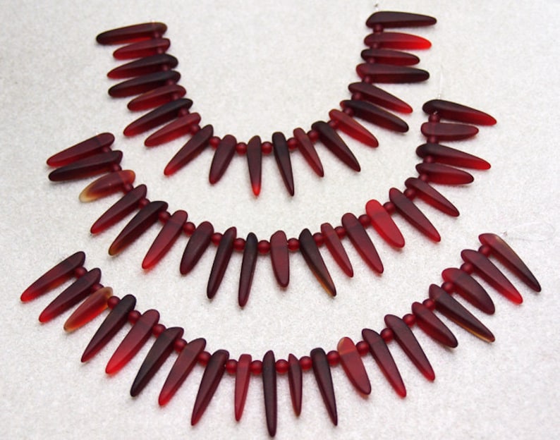 May include: Three strands of red glass beads, each strand is made up of teardrop-shaped beads with pointed tips.