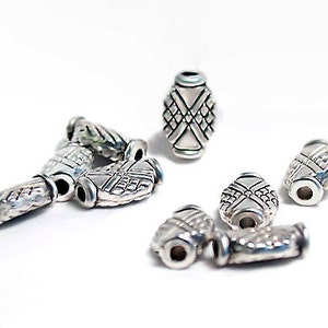 May include: A group of silver metal beads with a decorative design. The beads are oval shaped and have a textured surface.