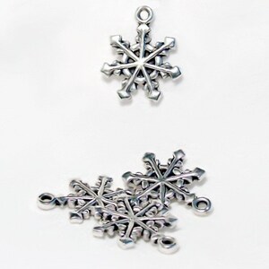 Op de afbeelding: Zilveren sneeuwvlokcharms met een lus om op te hangen. De charms zijn in verschillende maten en perfect voor het maken van sieraden of knutselen.