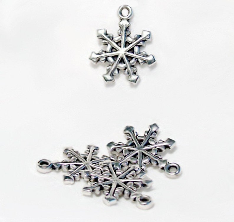 Op de afbeelding: Zilveren sneeuwvlokcharms met een lus om op te hangen. De charms zijn in verschillende maten en perfect voor het maken van sieraden of knutselen.