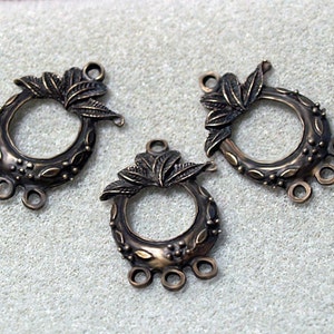 May include: Three antique bronze metal pendant charms with a leafy design and a circular opening. Each charm has four loops for attaching jewelry.