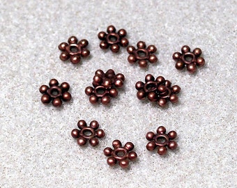 May include: A group of 10 small, brown, metal flower-shaped beads. The beads have a hole in the center and are designed for jewelry making.