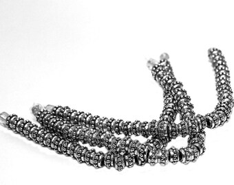 May include: A set of silver metal beads with a textured surface. The beads are strung together in a long chain.