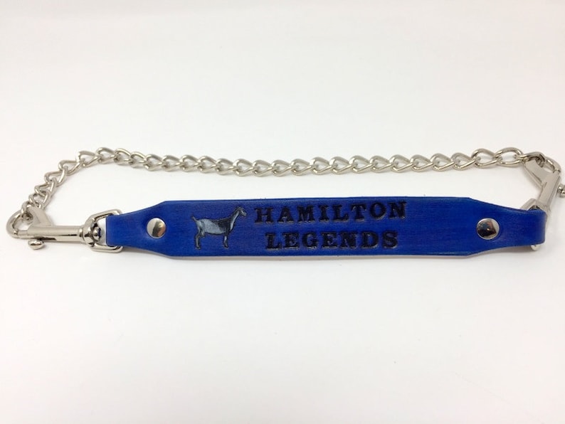 Pu&ograve; includere: Portachiavi in ​​cuoio blu con una catena argentata e un fermaglio argentato. Il cinturino in cuoio presenta una piccola silhouette di capra e il testo "HAMILTON LEGENDS" in rilievo in nero.