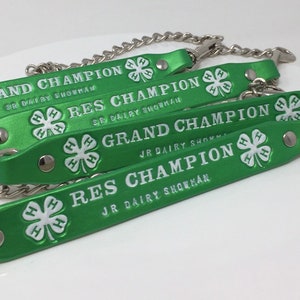 May include: Four green leather straps with silver chains and metal clasps. Each strap has a white four-leaf clover with the letters "H" printed on each leaf. The straps have white text that reads "Grand Champion", "Res Champion", "Grand Champion", and "Res Champion".