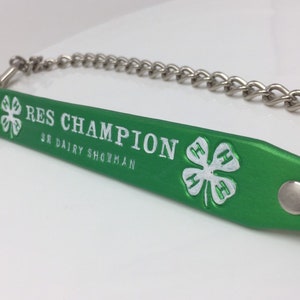 May include: Green leather showmanship halter with a silver chain and a white 4-H clover emblem. The halter has the text "RES CHAMPION SR DAIRY SHOWMAN" embossed in white.