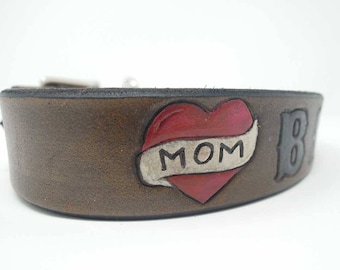 Op de afbeelding: Bruin lederen hondenhalsband met een rode harttattoo met de tekst "MOM" en een zwarte "B" aan de zijkant.
