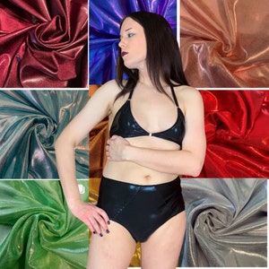May include: A black, shiny, high-waisted bikini bottom with a matching black, shiny, halter top. The bikini is shown against a backdrop of various iridescent fabrics.