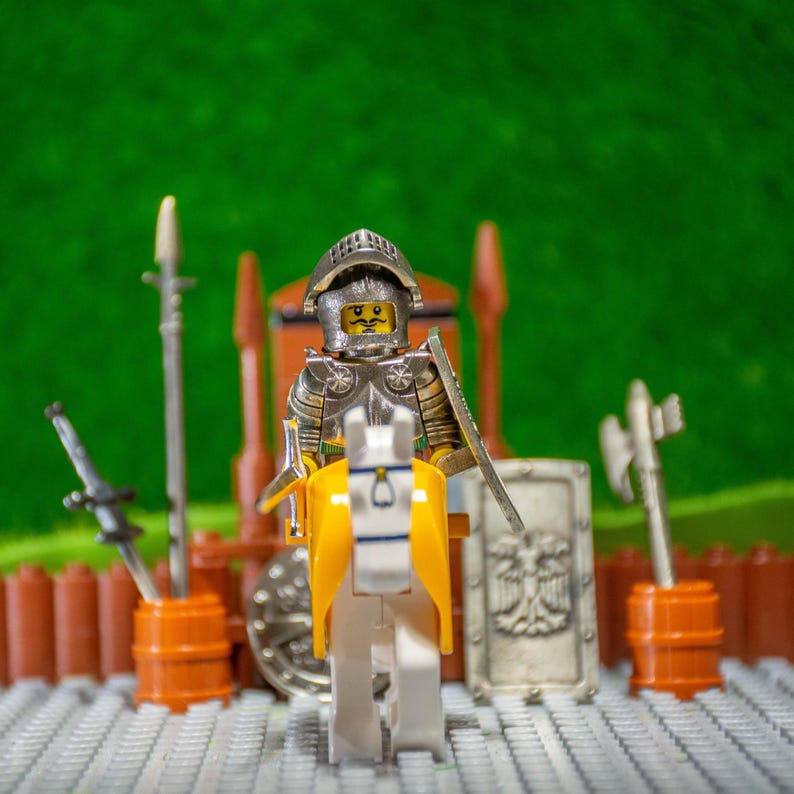 Puede incluir: Un caballero Lego con armadura plateada montando un caballo blanco con una silla amarilla. El caballero sostiene una espada y un escudo. El caballero est&aacute; de pie sobre una placa base Lego gris y blanca.