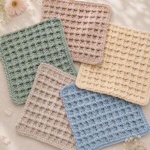 Può includere: Una collezione di cinque panni quadrati all'uncinetto caratterizzati da un motivo a rilievo a nido d'ape. I panni sono realizzati in tonalità tenui di rosa polvere, verde salvia, crema, beige e azzurro, con una trama a griglia uniforme.