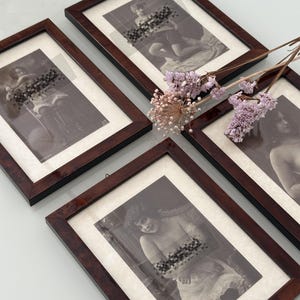 Può includere: Quattro stampe incorniciate in stile vintage con cornici in legno marrone scuro. Le immagini in bianco e nero raffigurano figure classiche, parzialmente oscurate da un effetto pixelato. Fiori rosa secchi sono disposti vicino alle cornici.