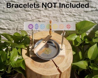 Könnte beinhalten: Ein Holzständer mit einer Metallschale und einem kleinen Räucherstäbchen. Eine durchsichtige Plastikkarte mit sieben bunten Chakra-Symbolen ist am Ständer befestigt. Der Text "Bracelets NOT Included" befindet sich oben im Bild.