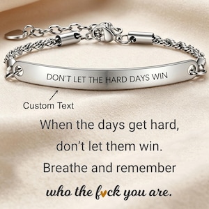 Może przedstawiać: Srebrzysta metalowa bransoletka z zakrzywioną, polerowaną blaszką z wygrawerowanym napisem "DON'T LET THE HARD DAYS WIN". Bransoletka posiada łańcuszek o splocie skręcanym, zapięcie typu karabińczyk oraz regulowany łańcuszek przedłużający.