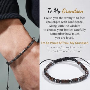Puede incluir: Se muestra una pulsera de cuentas marrón oscuro con detalles plateados. La pulsera está hecha de cuentas cuadradas de madera y cuentas cilíndricas de metal. El texto de la derecha dice "To My Grandson" y un mensaje de amor y orgullo.