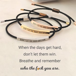 May include: Three black cord bracelets with metal bars engraved with the phrase "DON'T LET THE HARD DAYS WIN." The bars are in silver, gold, and rose gold. The image also includes the text "When the days get hard, don't let them win."