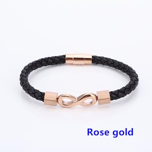 May include: A black leather bracelet with a rose gold infinity symbol charm and magnetic clasp. "Rose gold" is written below the bracelet.