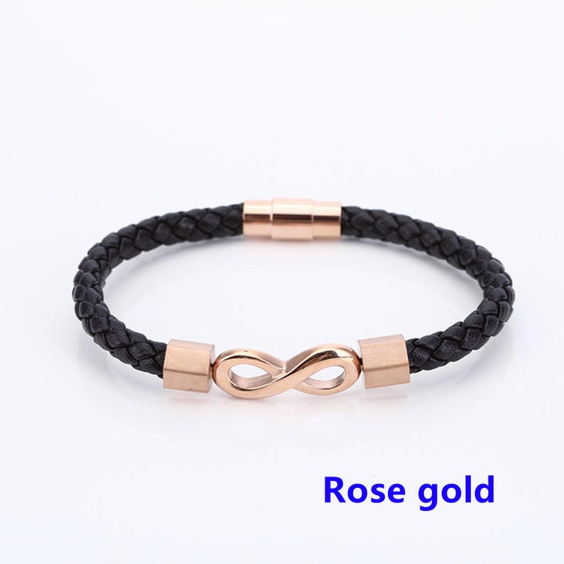 May include: A black leather bracelet with a rose gold infinity symbol charm and magnetic clasp. "Rose gold" is written below the bracelet.