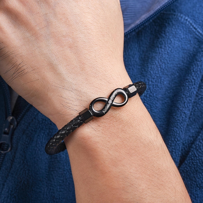 May include: A black leather bracelet with an infinity symbol charm. The charm is engraved with the text "Always & Forever".