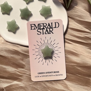 Pode incluir: Uma coleção de pedras em forma de estrela de aventurina verde em um prato branco, com um cartão que diz "Emerald Star" e "Green Aventurine, Luck + Opportunity + Growth". As pedras são de cor verde claro.