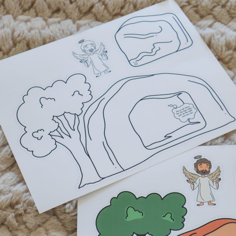 May include: White paper cutouts featuring line drawings of an angel, a tree, a cave, and a rock. One cutout has a speech bubble with text. The angel has a halo and wings. The tree is green. The cave is white with black outlines.