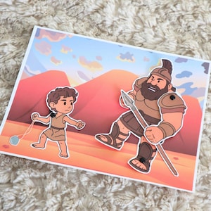 May include: A colorful illustration depicts a biblical scene with two figures. One figure is a young boy with a slingshot, and the other is a large warrior holding a spear. The background features a desert landscape with mountains and a blue sky with clouds.