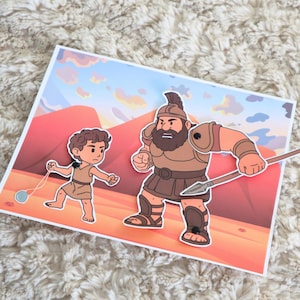 May include: A colorful illustration depicts a biblical scene with two figures. One figure is a young boy with a slingshot, facing a larger, armored warrior holding a spear. The background features a desert landscape with mountains and a sunset.