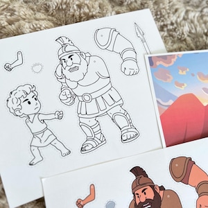 May include: Black and white illustrations of biblical characters, including a giant warrior and a young boy, are featured on paper cutouts. A spear and additional character pieces are also visible. The illustrations are designed for a children's craft project.