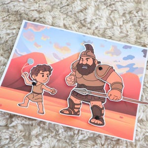 May include: A colorful illustration depicts a biblical scene with two cartoon figures. One figure is a young boy with a slingshot, and the other is a large warrior holding a spear. The background features a desert landscape with mountains.