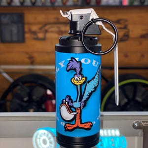May include: A blue and black grenade-shaped keychain with a cartoon Road Runner character on the side. The keychain has a white pull ring and the text "PLYMOUTH" on the side.