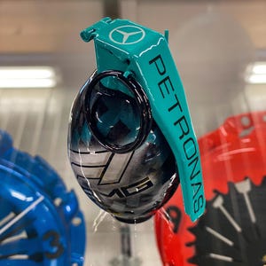May include: A teal and black grenade-shaped ornament with a Mercedes-Benz logo and the word "PETRONAS" on the side.