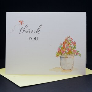 May include: A white thank you card featuring a red dragonfly and a watercolour illustration of a potted plant with pink flowers. The text "thank you" is written in black cursive.